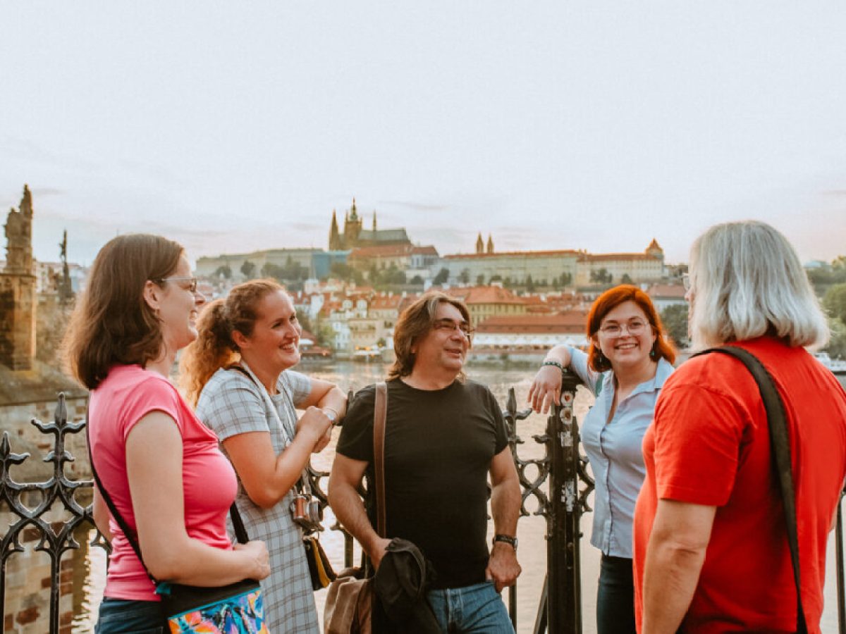 a group of tourists facing a tour guide on a walking tour of Prague, with a view of Prague Castle in the background