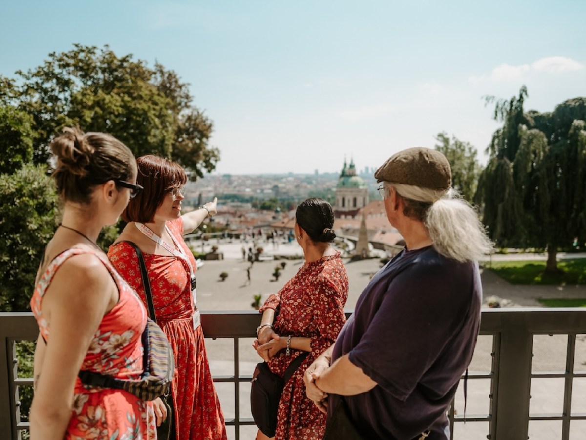 a tour guide pointing to St. Nicolas Church in front of a group of tourists on a Prague Castle tour